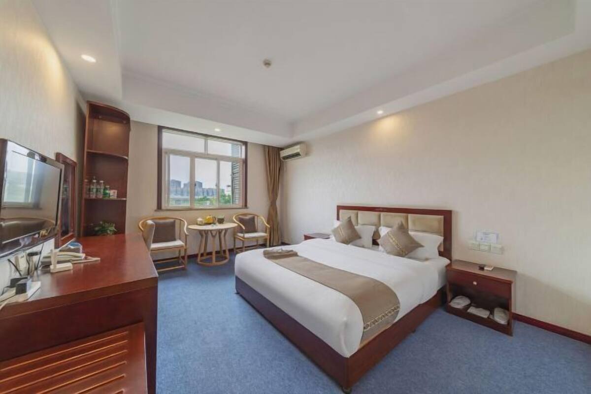 Een hotelkamer met een groot bed, een bureau met een televisie, een klein rond tafeltje en een stoel.