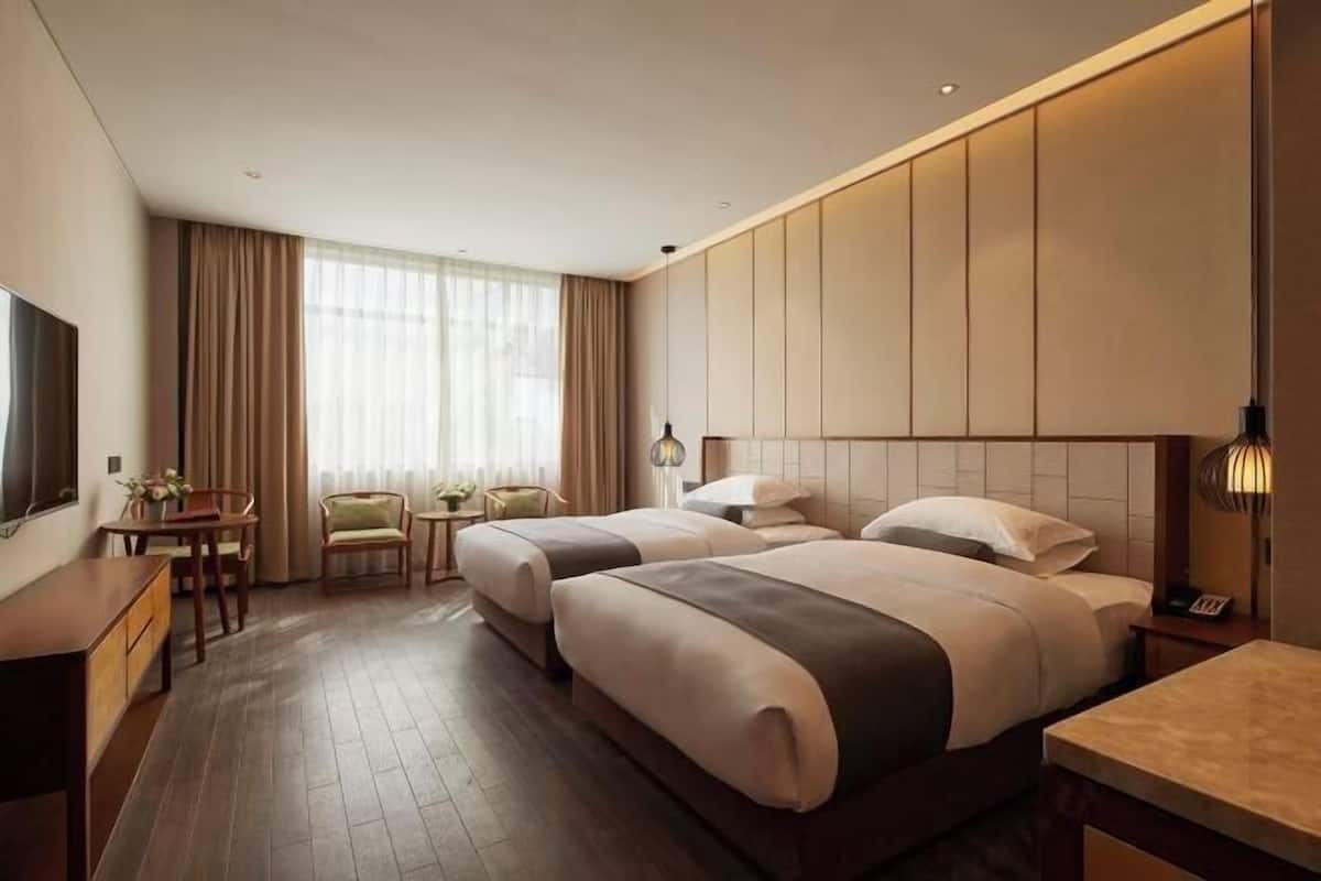 Een hotelkamer met twee bedden, een bureau, een stoel, een televisie en een raam met gordijnen.