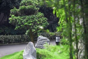 Jardim ajardinado com uma árvore conífera, uma rocha e um lança-chamas tradicional.