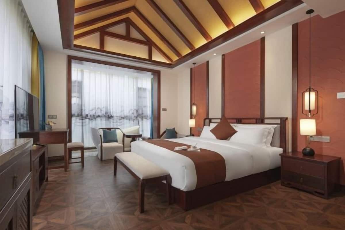 Een hotelkamer met een groot bed, nachtkastjes, een bureau, een stoel en een raam met gordijnen.