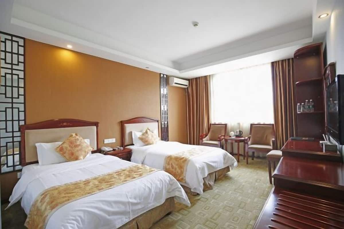 Een hotelkamer met twee bedden, een televisie, een bureau en een stoel.