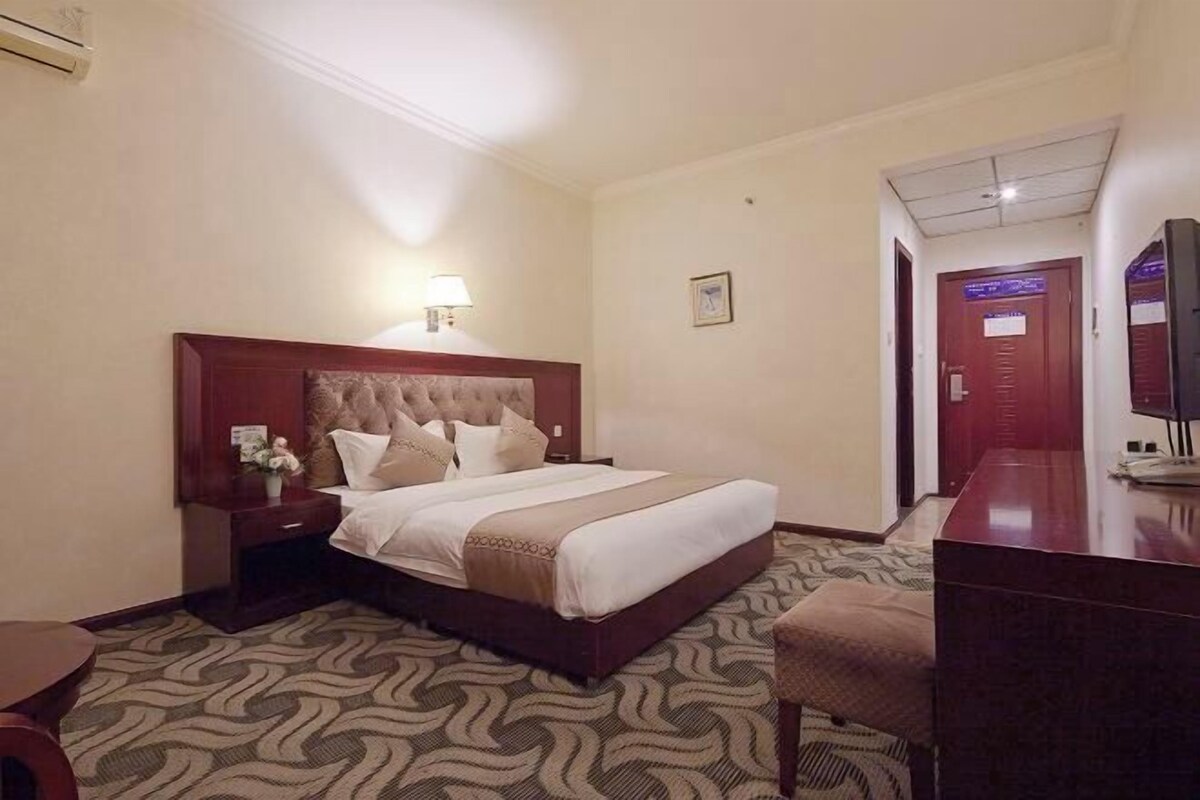 A hotel room with a large bed, a desk, a chair, a lamp, and a TV.