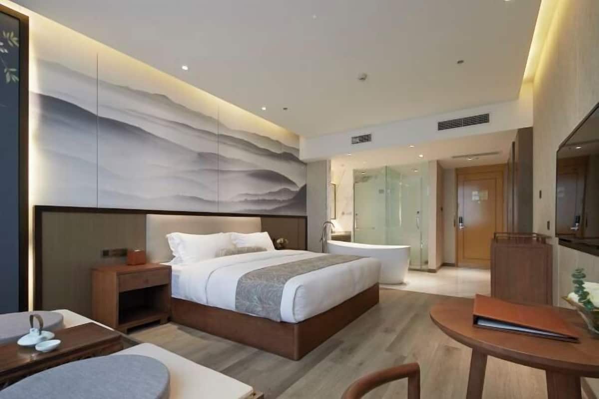 Een moderne hotelkamer met een groot bed, een aparte badkamer, een zithoek en uitzicht op de skyline.