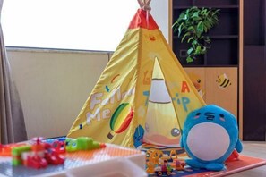 Un espace de jeux avec une tente jaune sur laquelle est écrit « Suivez-moi », un jouet en peluche bleu et divers autres jouets disposés sur un tapis.