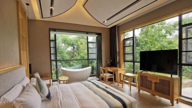 A bedroom with a large bed, a desk, a TV, and a bathtub. - Haitian Yongxin Hotel (Qionglai)