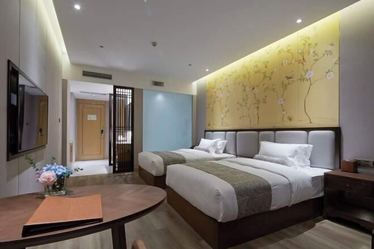 Een hotelkamer met twee bedden, een televisie, een bureau en een decoratieve wand.