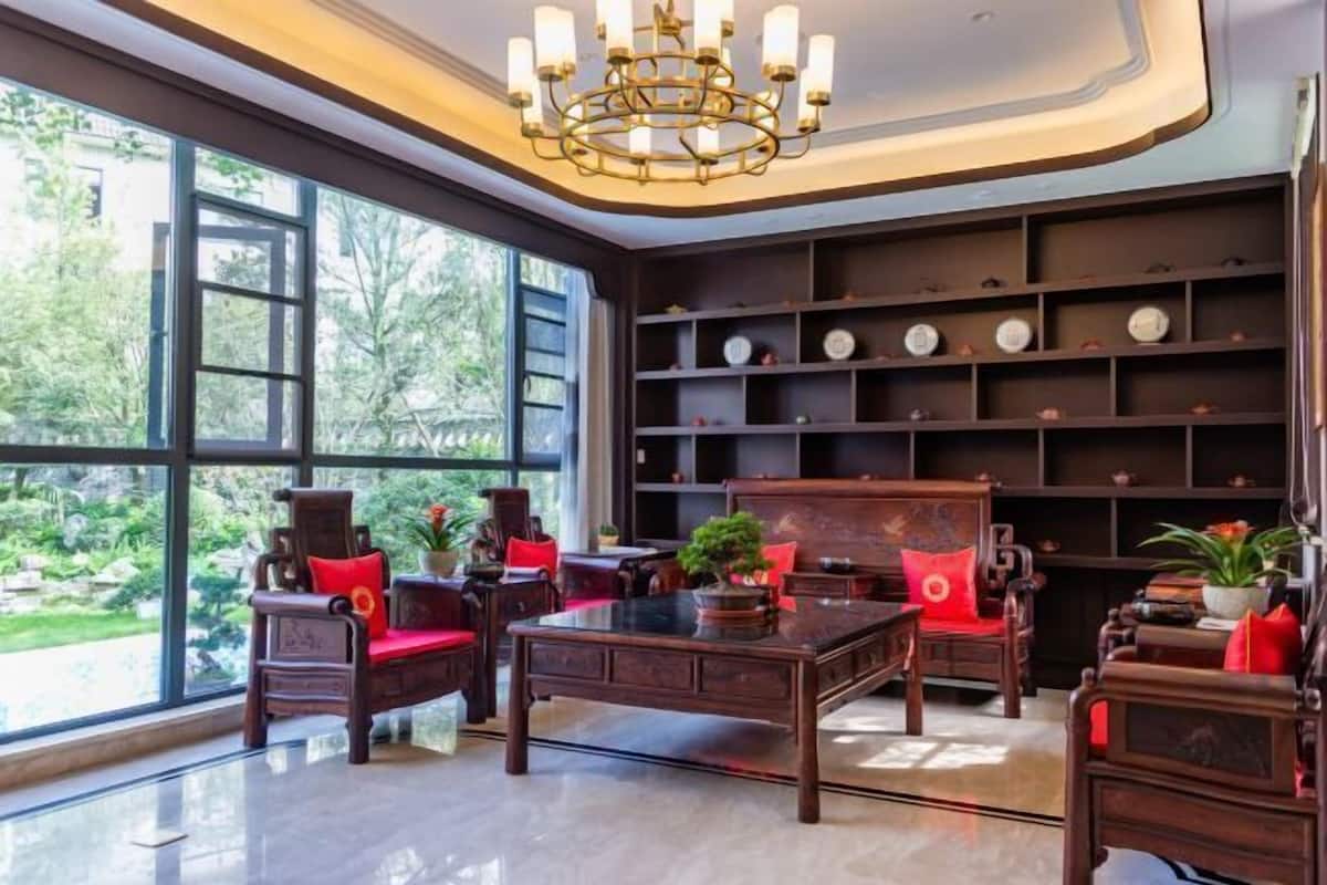 Een ruime kamer met grote ramen, een kroonluchter en een boekenkast.