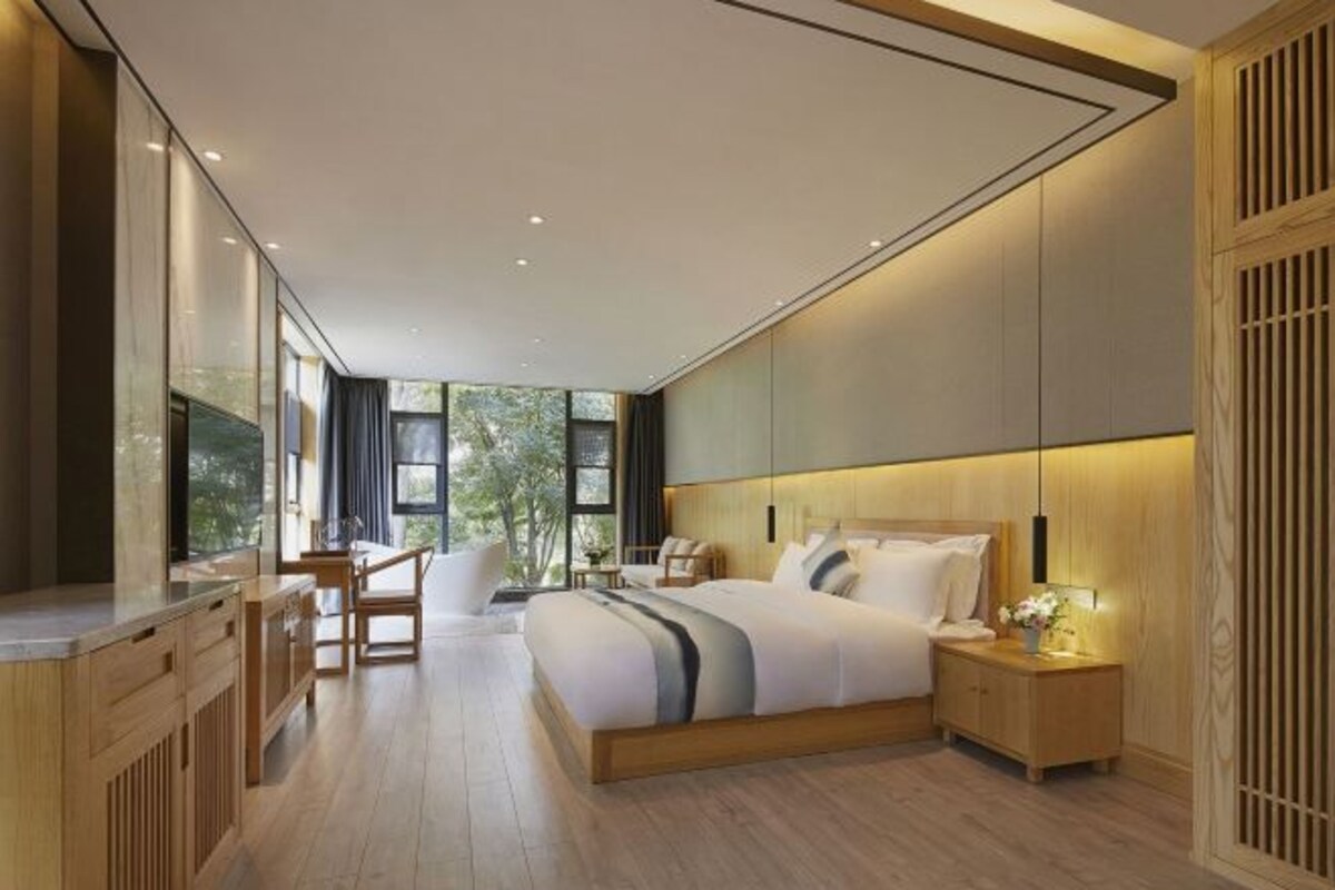 Une chambre moderne avec un grand lit, des tables de chevet, un bureau et une vue sur la verdure.