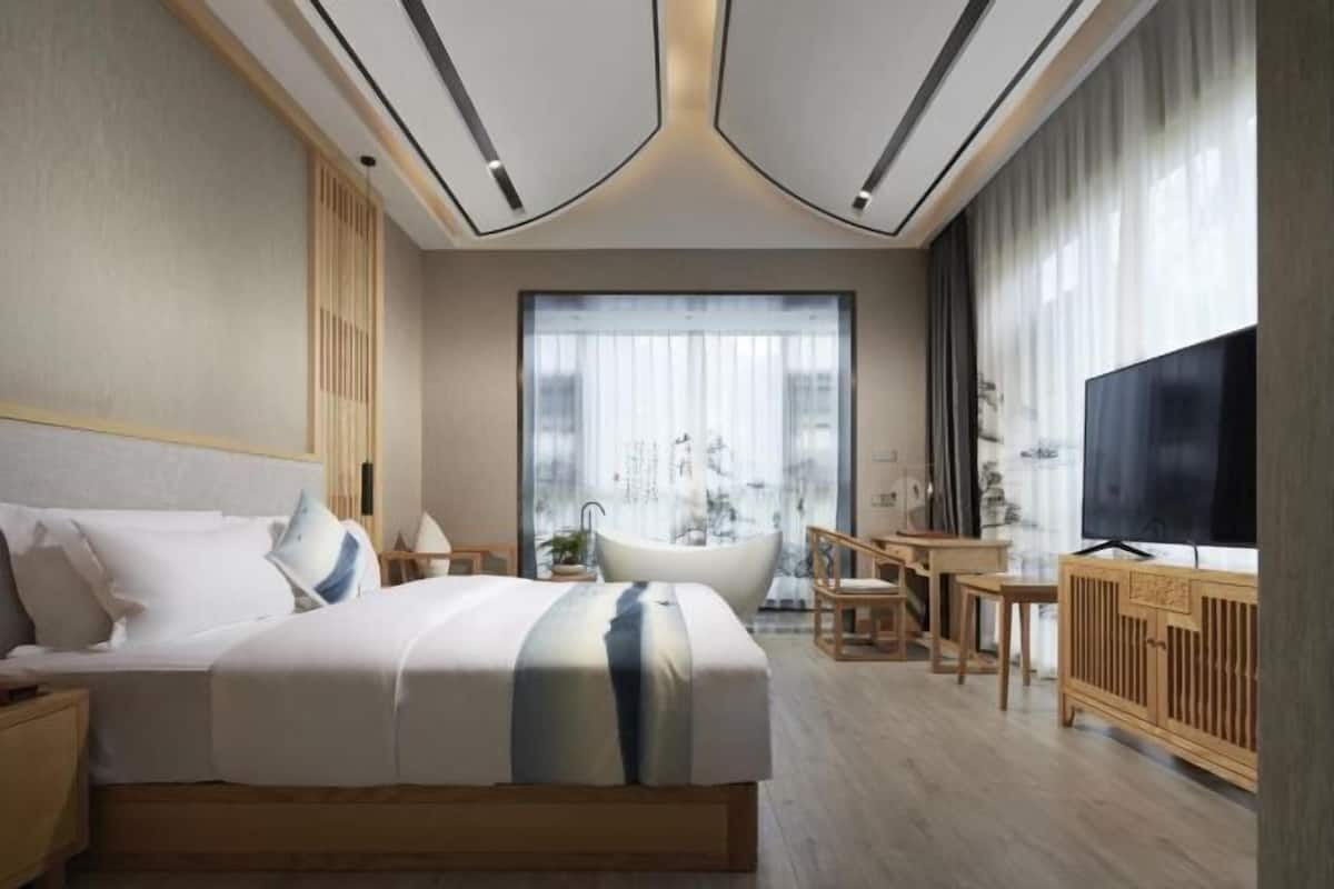 Een moderne hotelkamer met een groot bed, een badkuip, een televisie en uitzicht op de stad.
