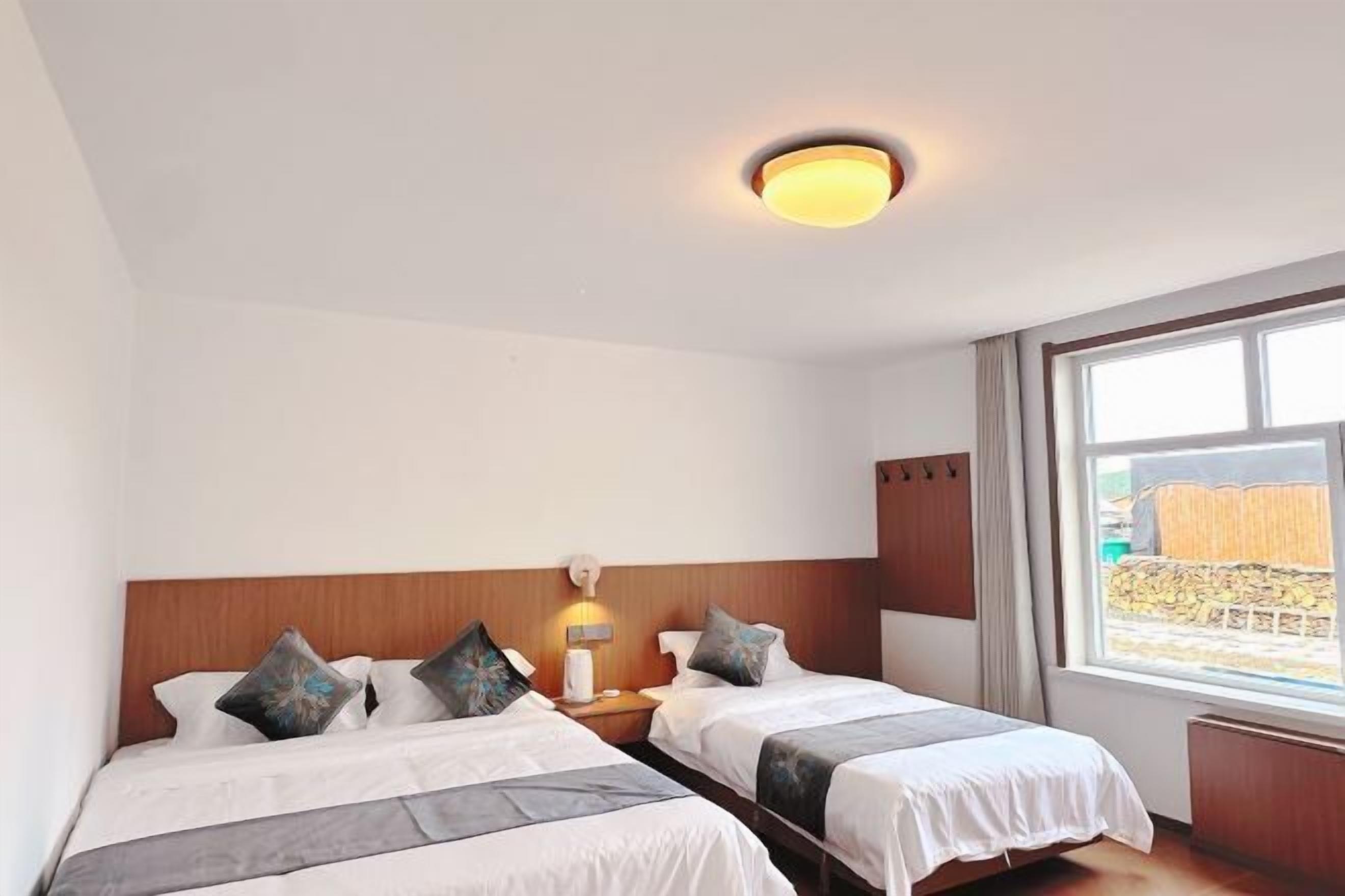 Une chambre d’hôtel avec deux lits, une table de chevet, une lampe et une fenêtre donnant sur un beau paysage.