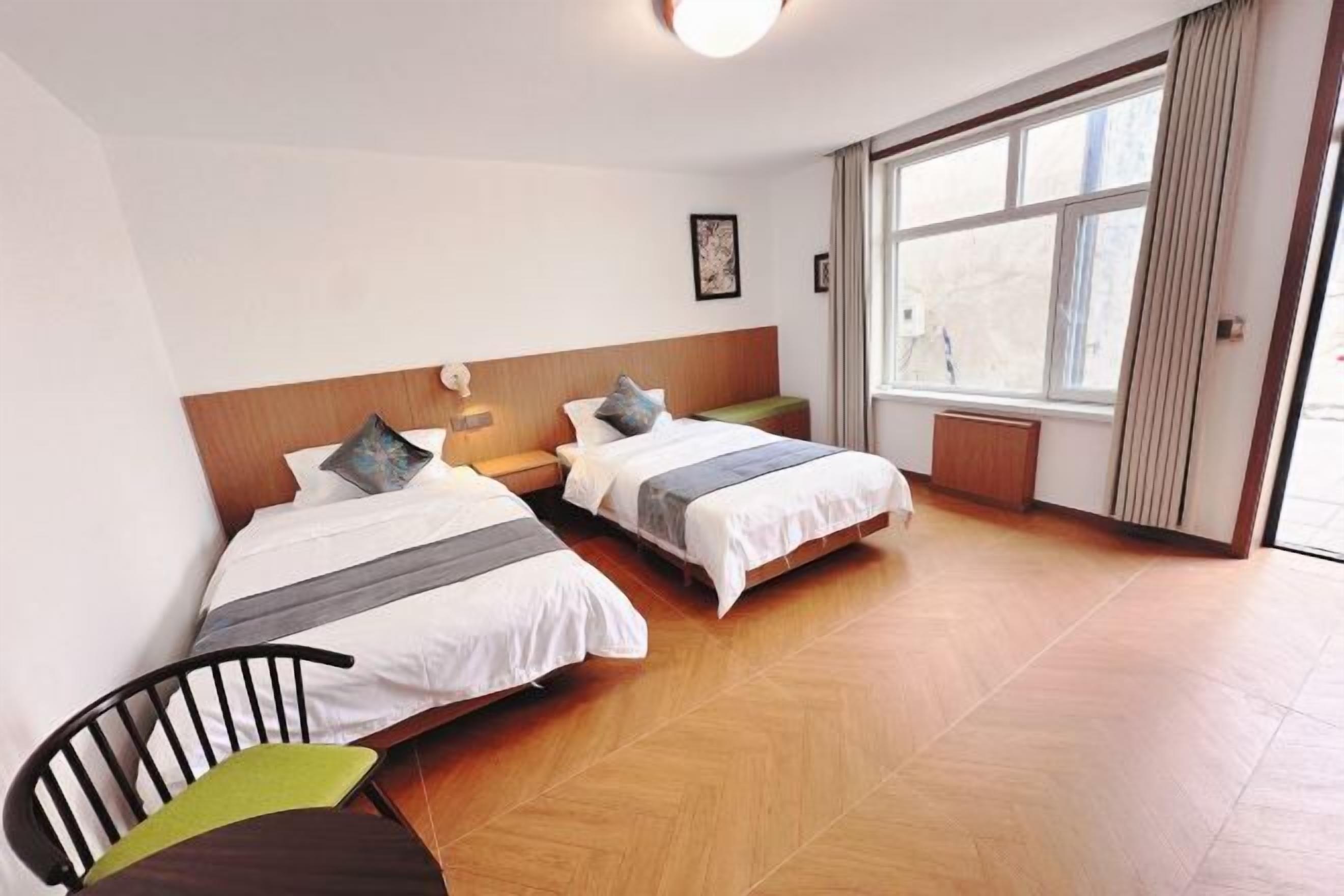 Une chambre d’hôtel avec deux lits, une chaise, une petite table et une grande fenêtre.