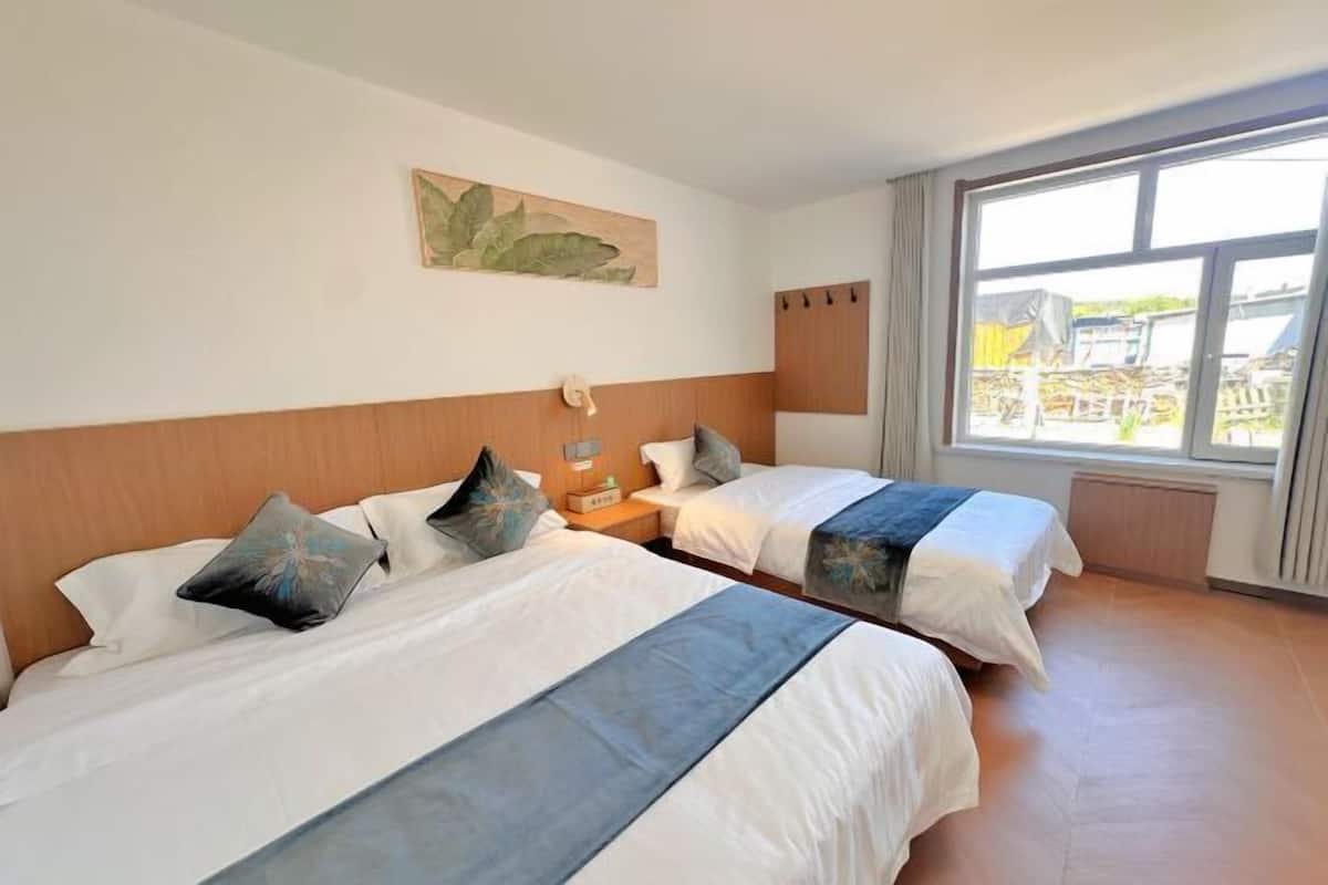 A hotel room with two beds, a large window, and a painting on the wall.