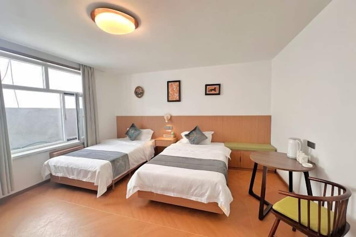 A hotel room with two beds, a small table, a chair, and a window.