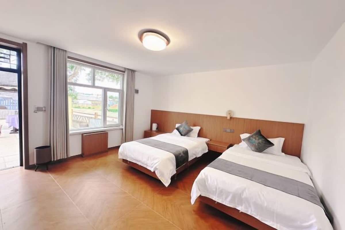 A hotel room with two beds, a large window, and a view of the outside.