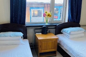 Habitación de hotel con dos camas individuales, una mesita de noche de madera con un hervidor y una ventana con vistas al exterior.