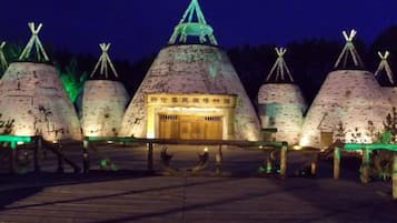A row of traditional conical structures with a central building, possibly a museum or cultural exhibit, and a wooden walkway in front.