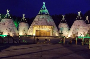 A row of traditional conical structures with a central building, possibly a museum or cultural exhibit, and a wooden walkway in front.