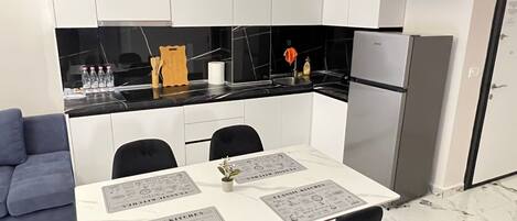 A modern kitchen with white cabinets, a black countertop, and a stainless steel refrigerator. There is a dining table with black chairs and a menu on the table.