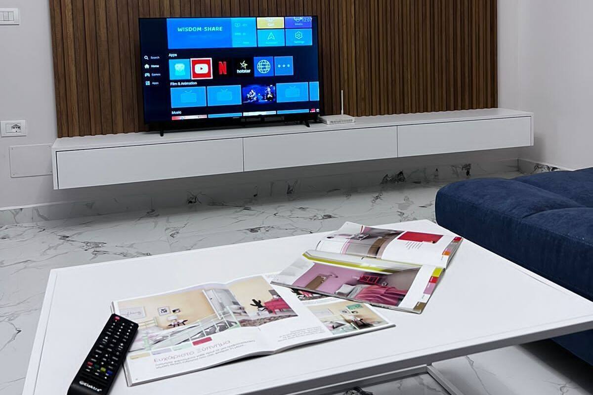A modern living room with a flat-screen TV mounted on a white shelf, a remote control, and a magazine on a white coffee table.