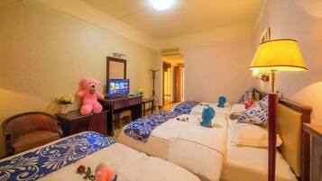 A hotel room with two beds, a desk with a computer, a teddy bear, and a lamp.