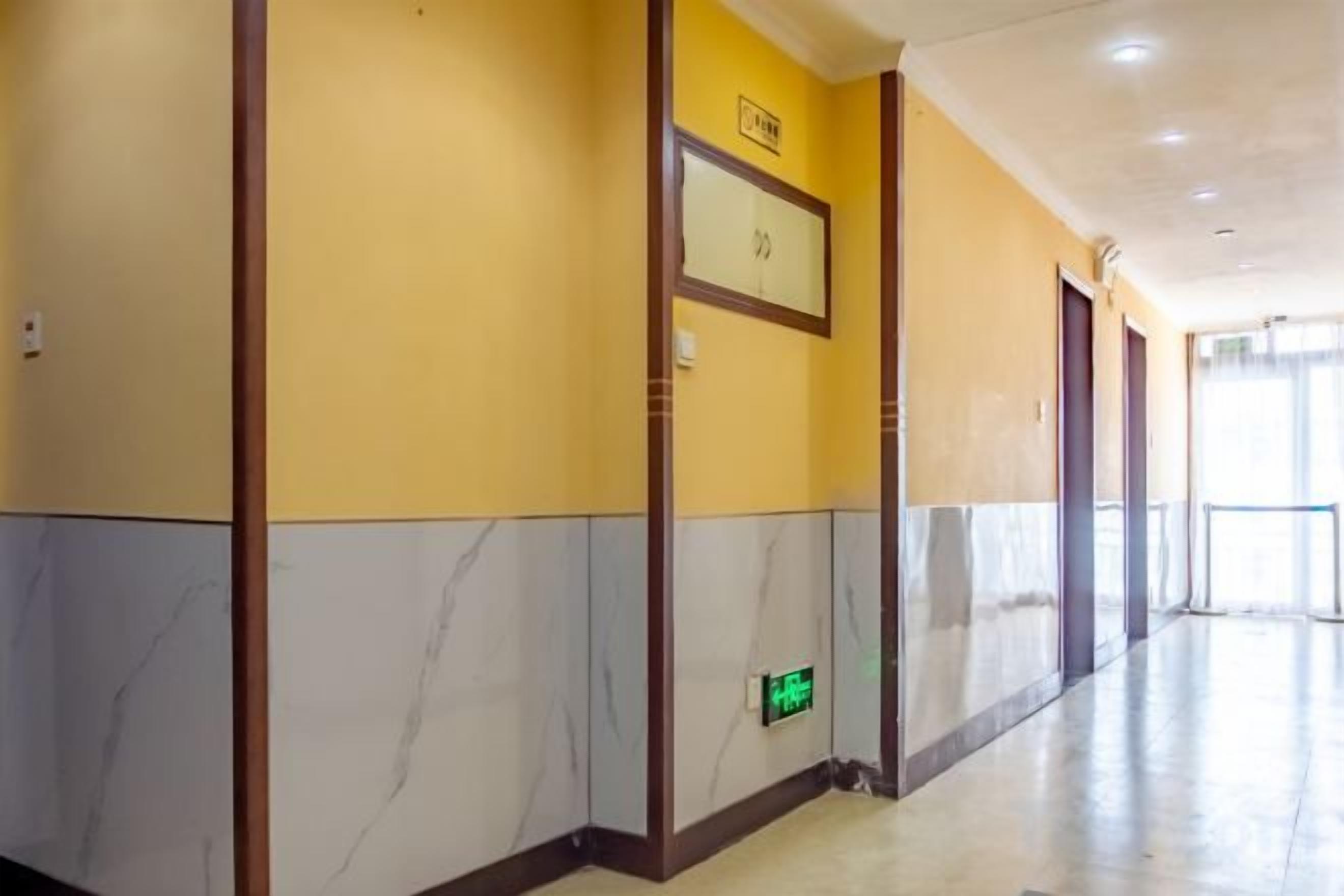Un pasillo de hotel con piso de mármol, puertas de madera y una señal de salida verde.