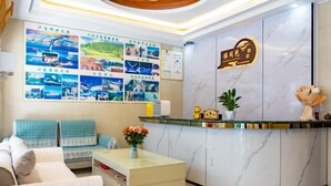Een hotel receptie met een marmeren balie, een zithoek met een bank en fauteuils, en een muur versierd met diverse foto's.