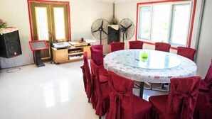 A dining area with a round table, red chairs, a small stage with musical equipment, and two standing fans.