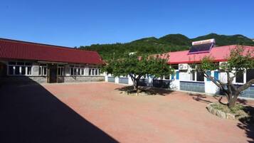 A building with a red roof, a paved courtyard, and a tree.