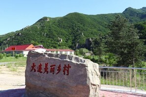 Un grand rocher sur lequel est gravé du texte, un bâtiment avec un toit rouge et un paysage montagneux.