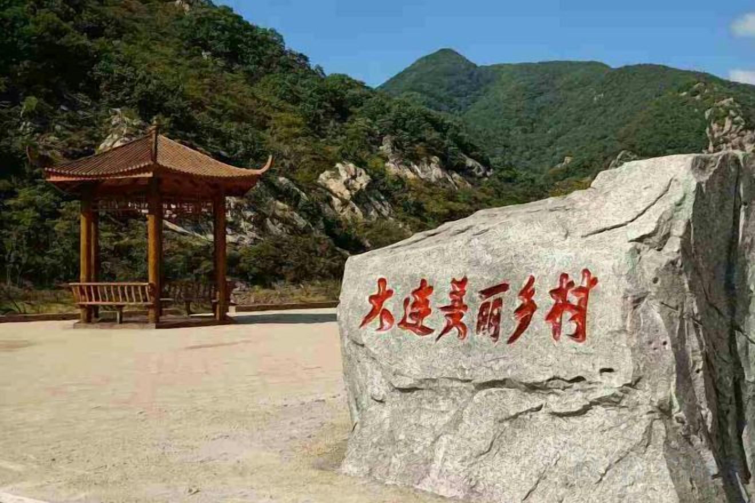 A rock with carved text, a pavilion, and a mountainous backdrop.