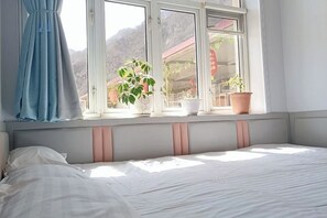 Una habitación con cama, ventana con cortinas y plantas en macetas sobre el alféizar.