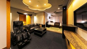 Quarto de hotel moderno com cadeira de massagem, sofá, TV de tela plana e uma janela grande.