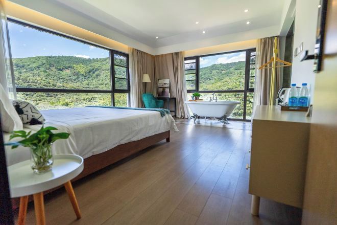 Une chambre à coucher avec un lit, une petite table sur laquelle est posée une plante, une baignoire et une vue sur un paysage verdoyant.
