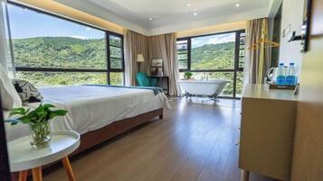 Une chambre à coucher avec un lit, une petite table sur laquelle est posée une plante, une baignoire et une vue sur un paysage verdoyant.