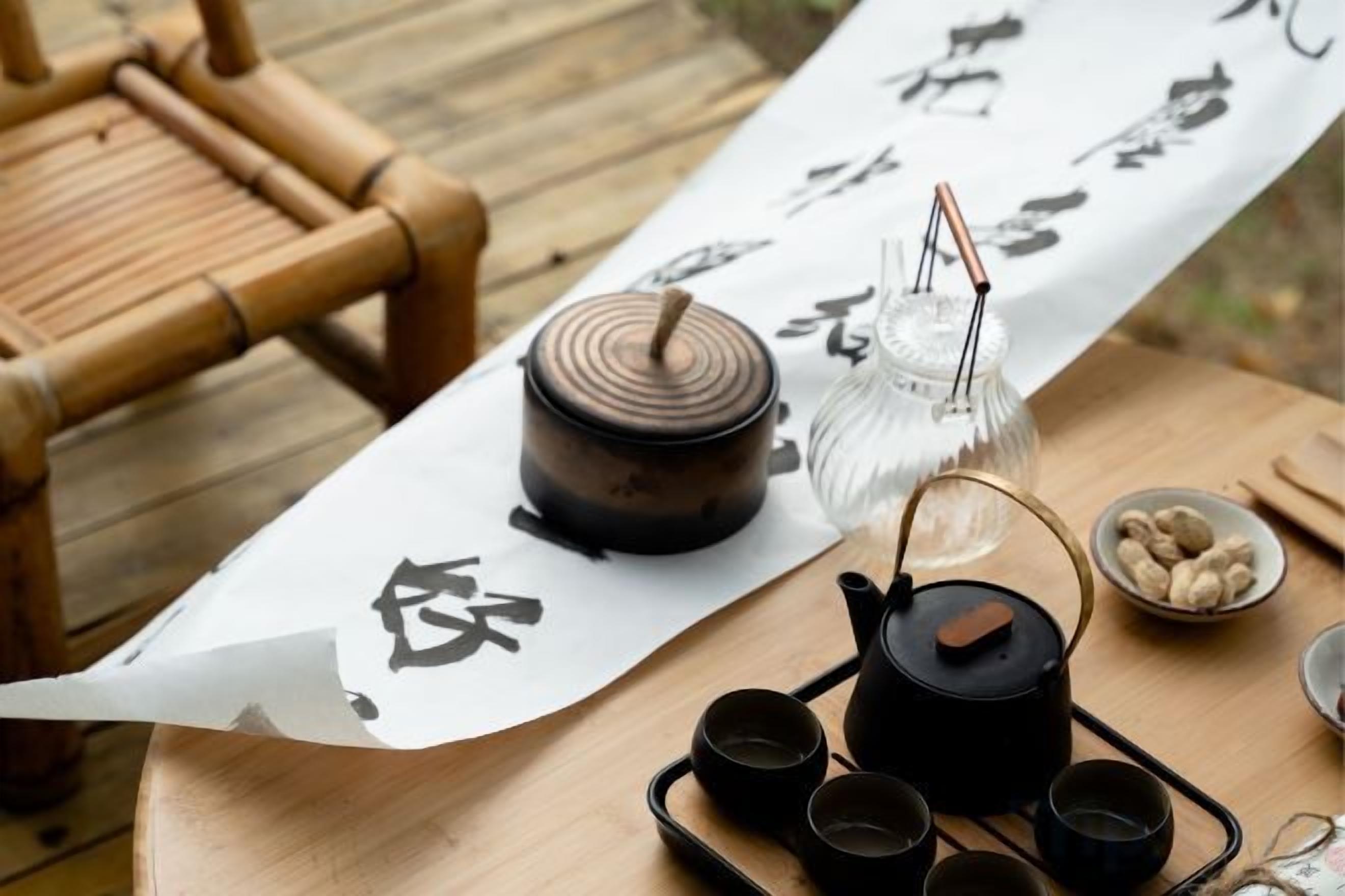 A table with a teapot, cups, and a decorative item on a tablecloth with calligraphy.