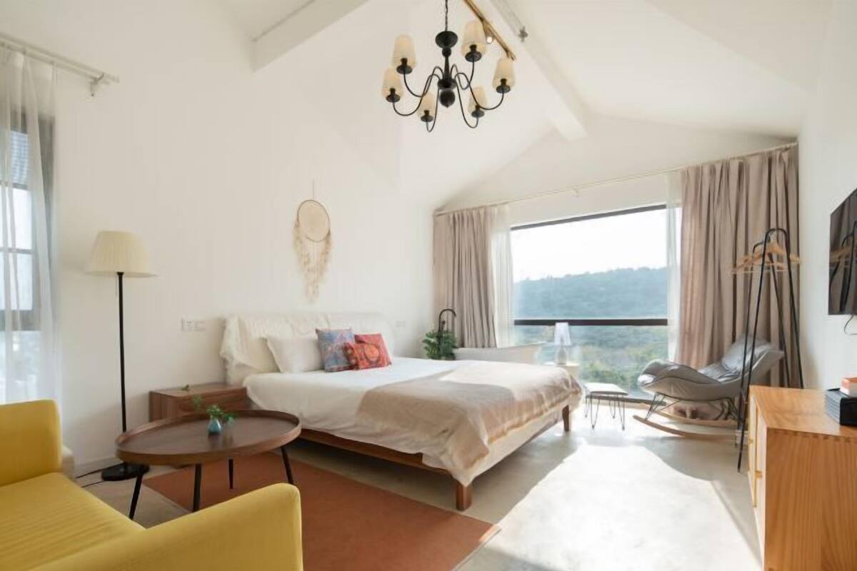 A modern bedroom with a large bed, a desk, a chair, and a view of the outdoors.