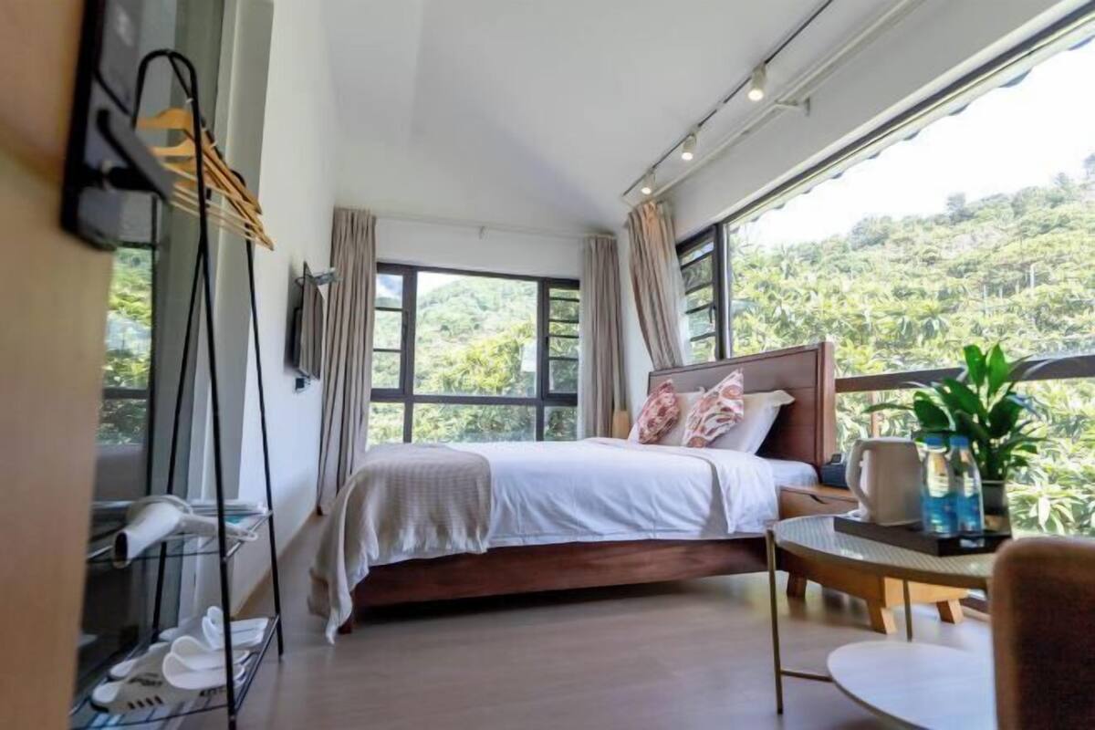 A bedroom with a bed, a table, and a view of a lush green landscape.