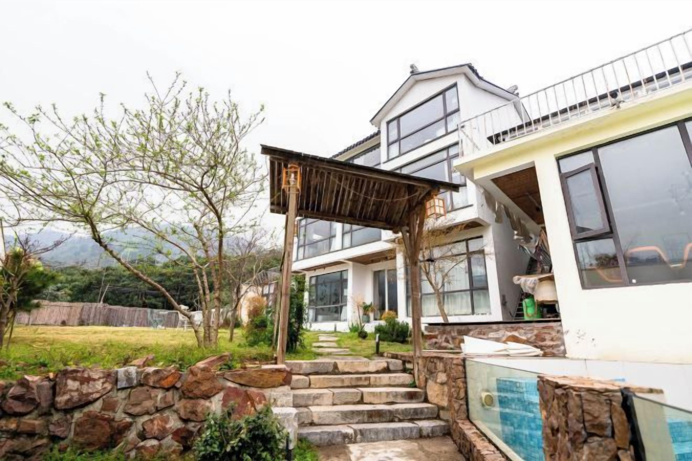 A modern house with a stone staircase leading to a wooden deck, a large window, and a view of the surrounding landscape.