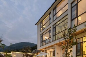 A multi-story building with balconies and large windows, surrounded by trees and a mountainous backdrop. - Carefree Valleys (Suzhou Qiyuan Road Store) (Suzhou)