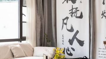 A room with a sofa, a vase with flowers, and a large wall with calligraphy.