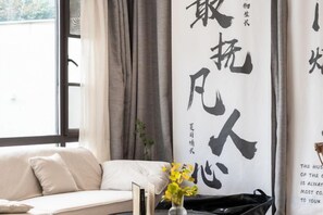 A room with a sofa, a vase with flowers, and a large wall with calligraphy. - Carefree Valleys (Suzhou Qiyuan Road Store) (Suzhou)