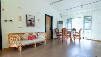 A spacious room with a wooden floor, a wicker sofa, and a dining table with chairs.