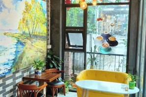 A dining area with a table and chairs, a yellow sofa, and a large window with a view of the street.