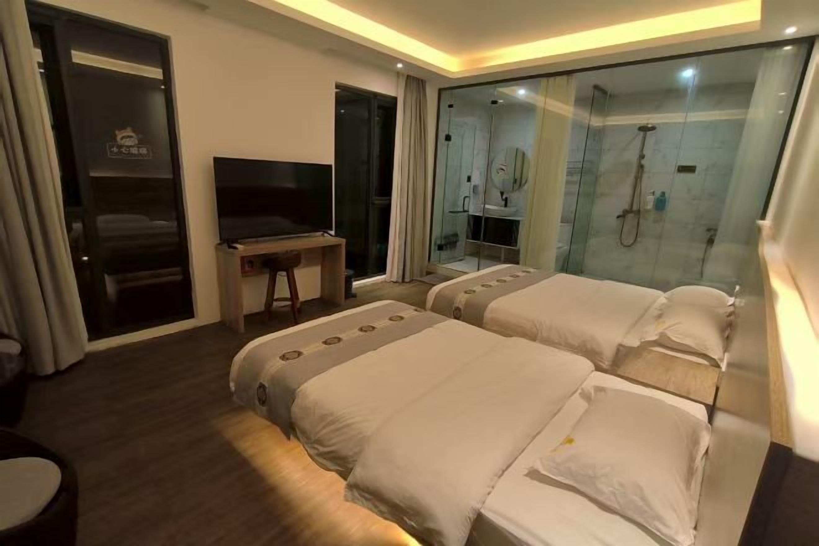 Habitación de hotel con dos camas, televisión, escritorio y cabina de ducha acristalada.