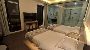 Habitación de hotel con dos camas, televisión, escritorio y cabina de ducha acristalada.