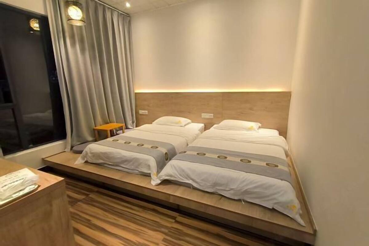 Une chambre d’hôtel avec deux lits, une tête de lit en bois, une petite table et une fenêtre avec des rideaux.