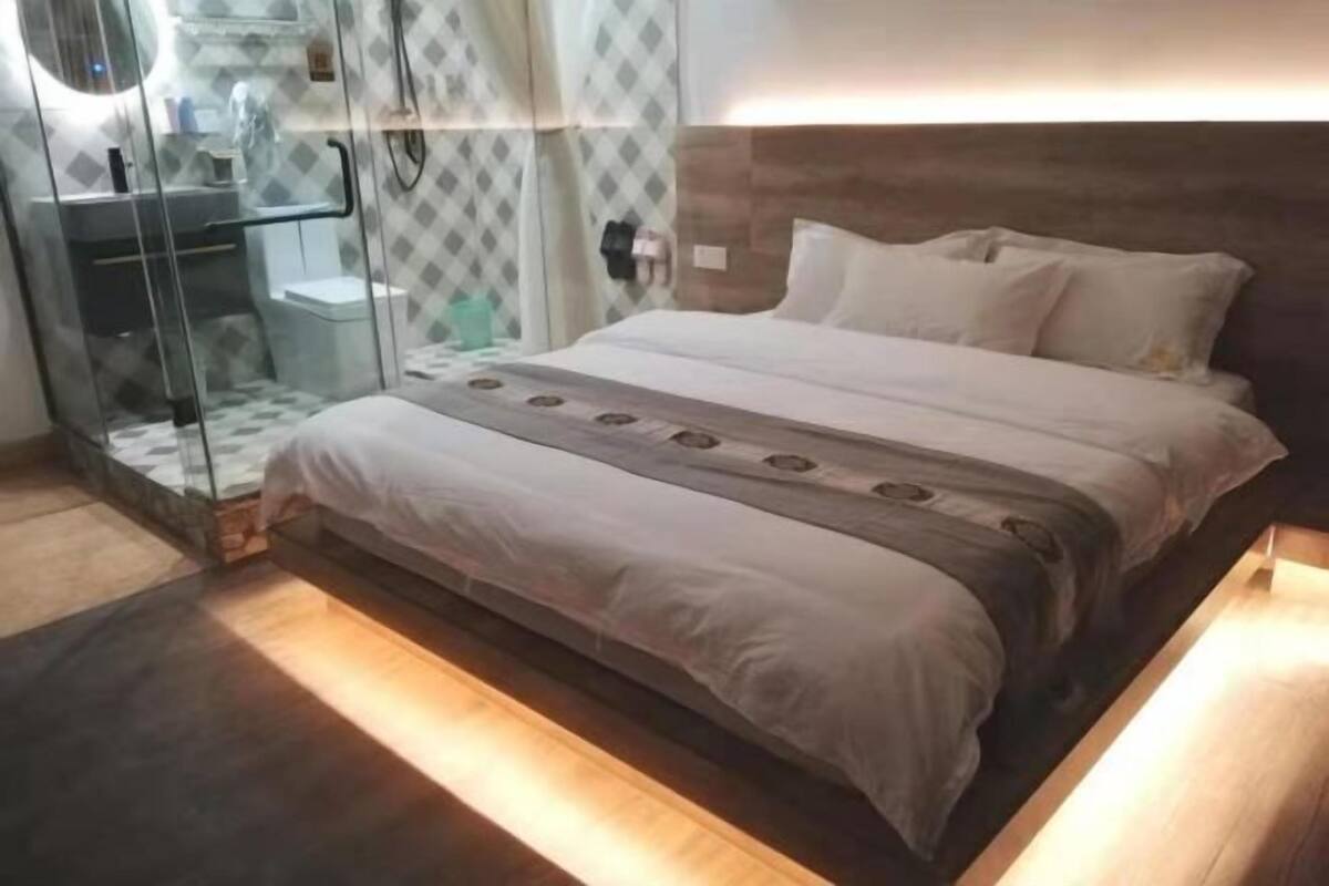 Une chambre à coucher moderne avec une cabine de douche en verre, une tête de lit en bois et un lit parfaitement fait.
