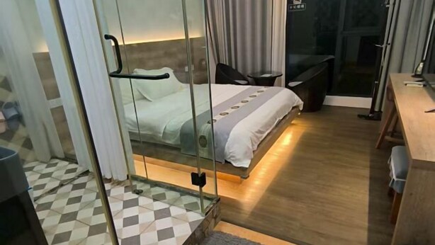 A hotel room with a bed, a desk, a chair, a small table, and a glass partition. - Miyuanju Farm House (Guangzhou)