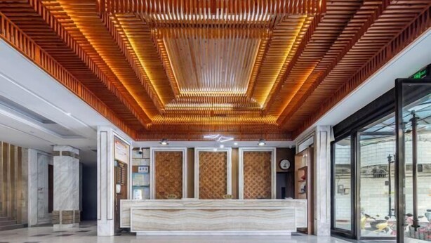 Um saguão de hotel moderno com teto de madeira, balcão de recepção de mármore e grandes portas de vidro.