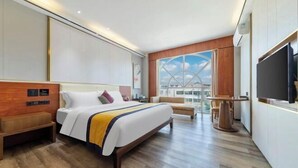 Quarto de hotel moderno com uma cama grande, área de estar, televisão e vista para a cidade.